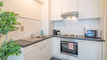 Una cocina moderna con armarios blancos, una estufa de acero inoxidable, un microondas y un hervidor.