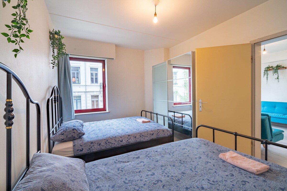 Un dormitorio con dos camas, una ventana, un espejo y una puerta que da a otra habitación.