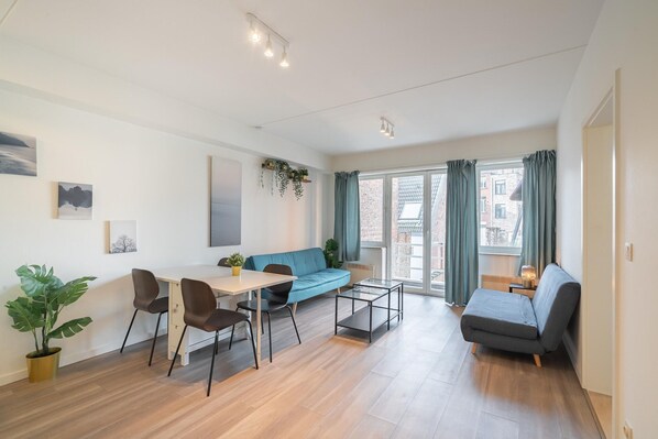 Una sala de estar moderna con un sofá, una mesa de comedor, sillas, una mesa auxiliar y una planta en maceta.
