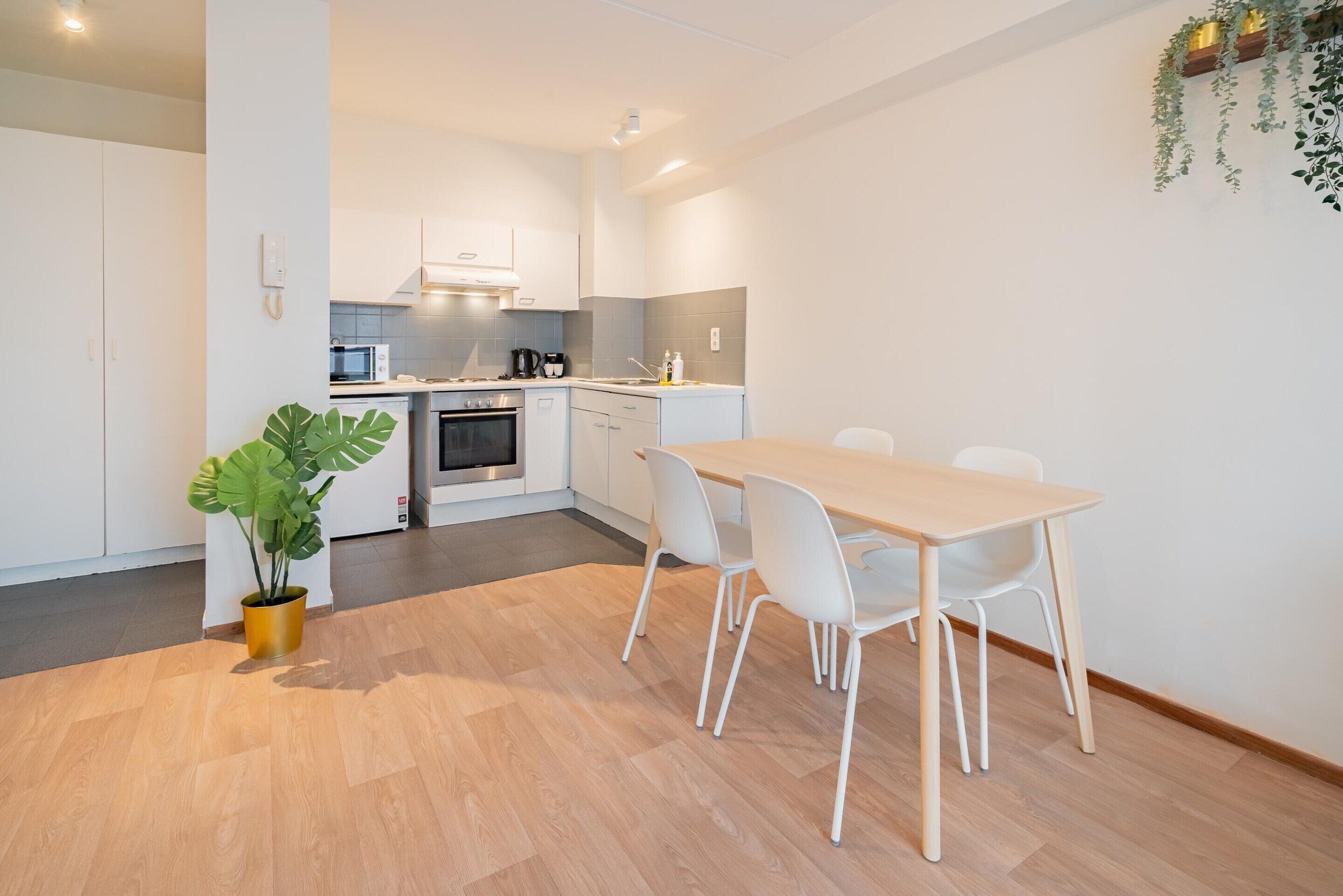 Een moderne keuken met witte kasten, een eettafel met stoelen en een potplant.