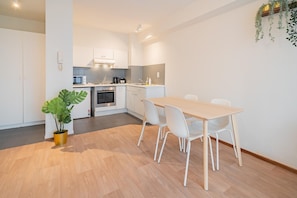 A modern kitchen with white cabinets, a dining table with chairs, and a potted plant.