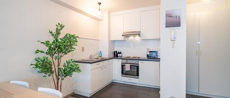 A modern kitchen with white cabinets, a built-in oven, and a small dining table.