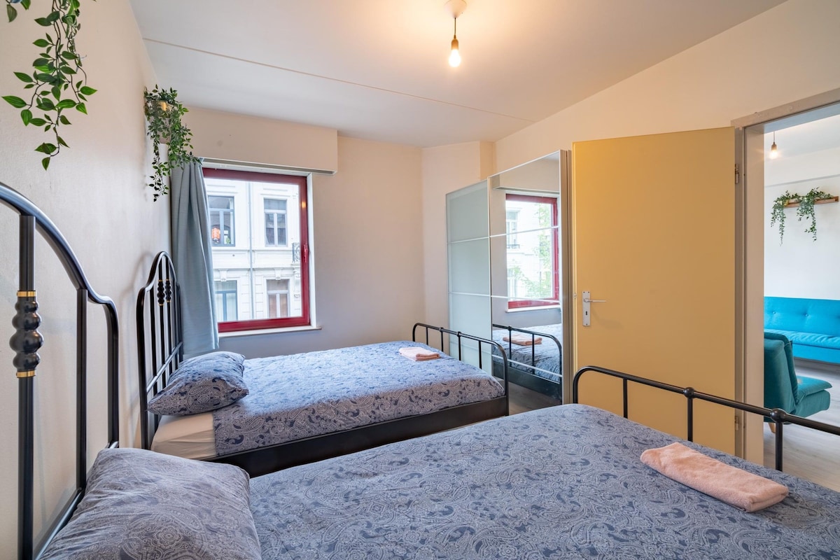 Un dormitorio con dos camas, una ventana, un espejo y una puerta que da a otra habitación.