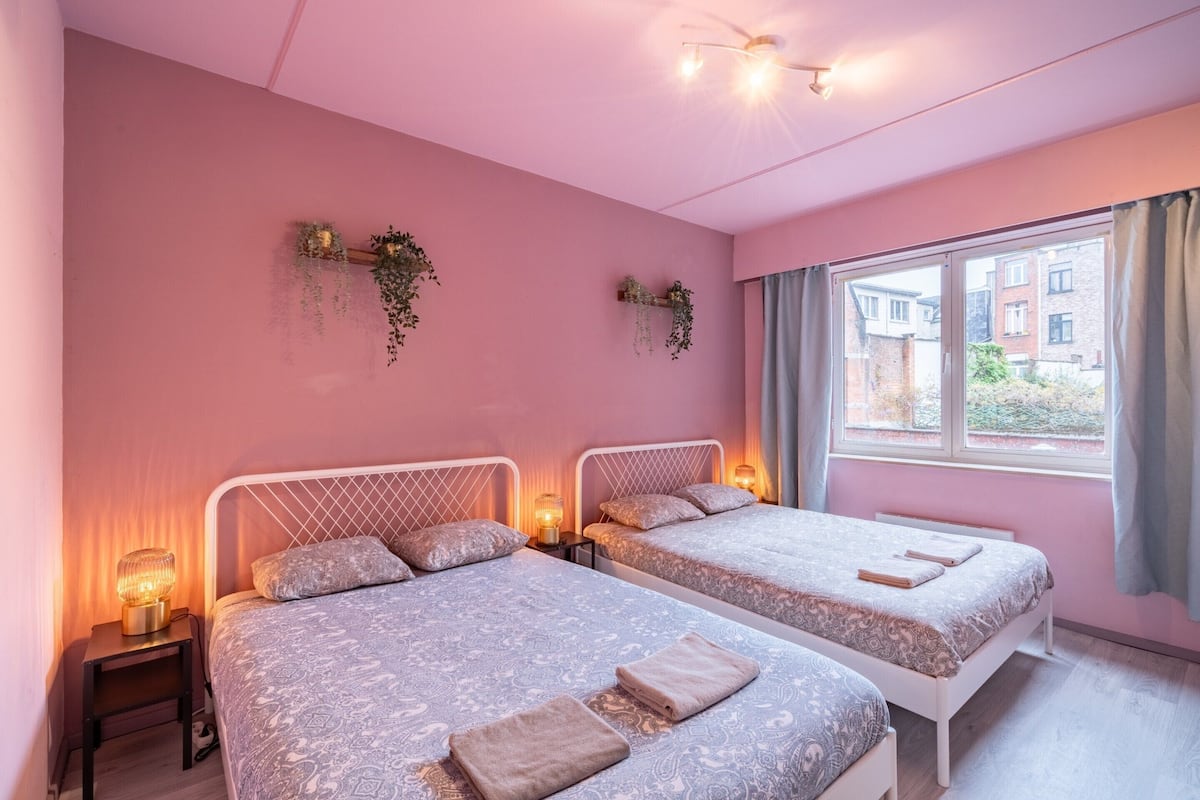 Un dormitorio con dos camas, lámparas de noche y una ventana con cortinas.