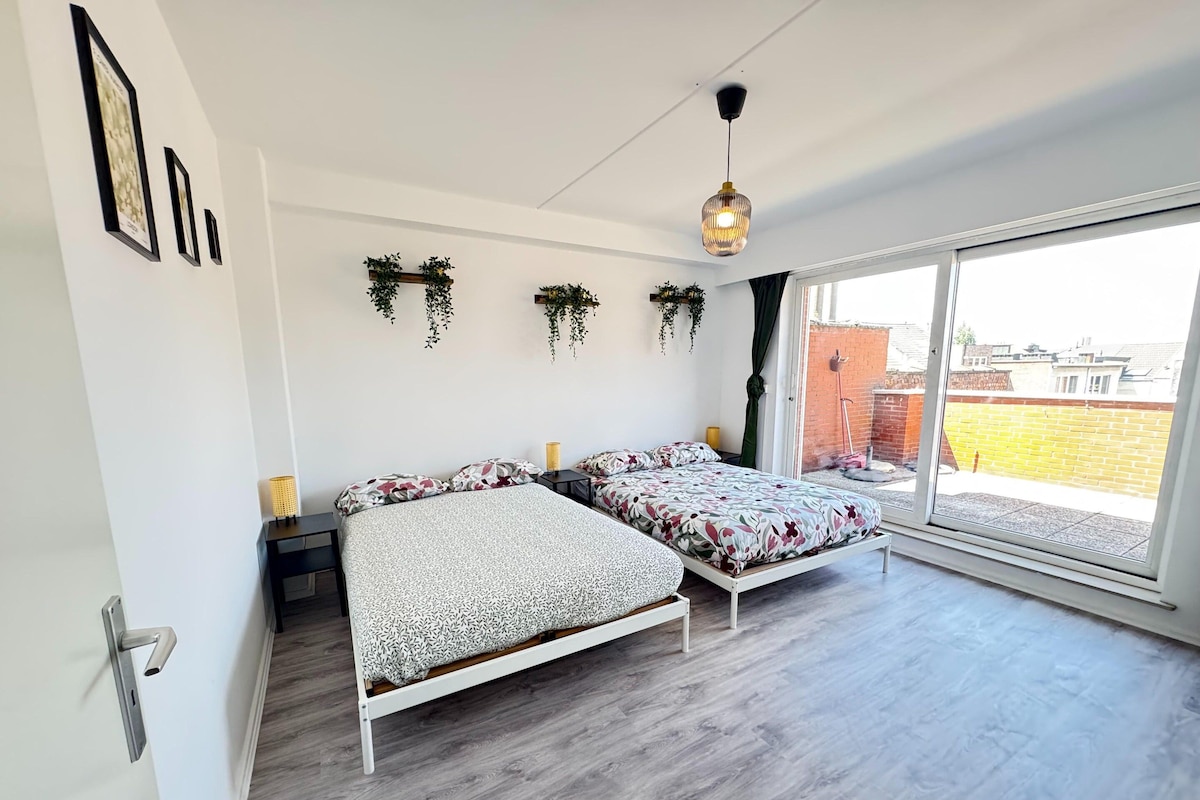 A bedroom with two beds, a large window, and hanging plants.