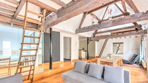 A modern interior with exposed wooden beams, a grey sofa, a wooden ladder, and a dining area. - Temple Triplex Spacious Apartment (Antwerp)