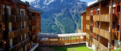 Ein Holzgebäude mit mehreren Balkonen, einem Kiesweg und Blick auf die Berge.