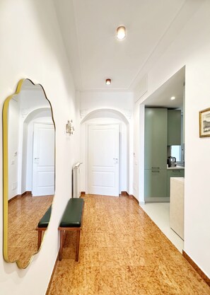 Un pasillo con un banco, un espejo grande y una puerta que da a una zona de cocina.