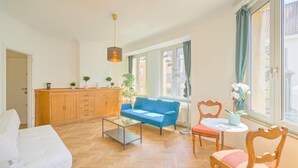 Een woonkamer met een bank, een salontafel, een houten kast, een wit bed en een raam met gordijnen.