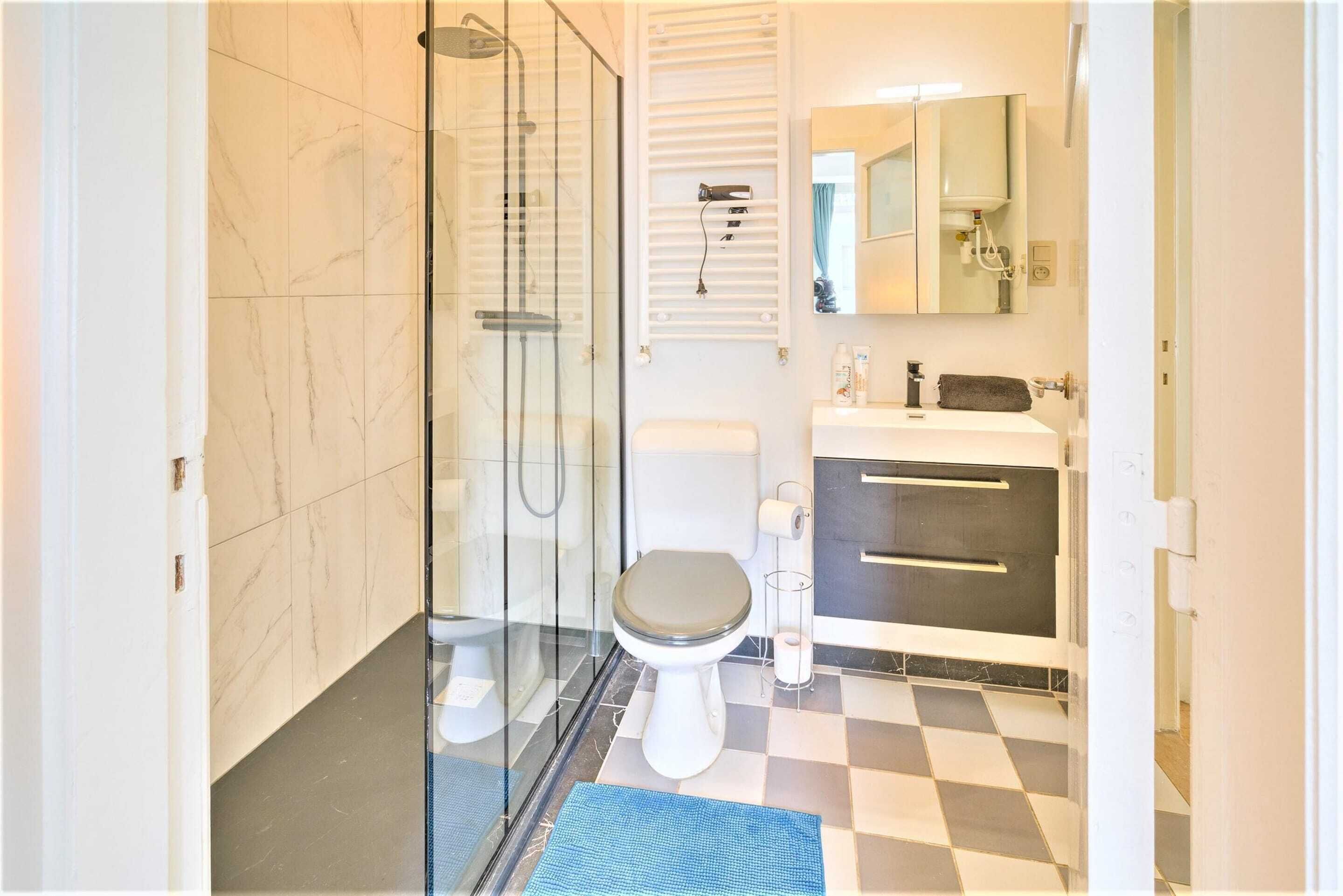Un baño con ducha acristalada, inodoro, lavamanos con espejo y suelo a cuadros.