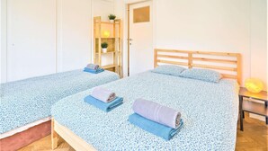 Een kamer met twee bedden, een houten hoofdbord, een tafeltje met een lamp en een plank met planten.