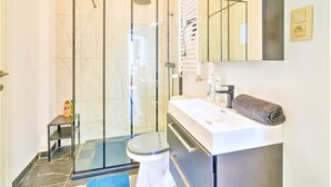 Een badkamer met een douchecabine van glas, een wit toilet, een wastafel met een handdoek en een spiegel.