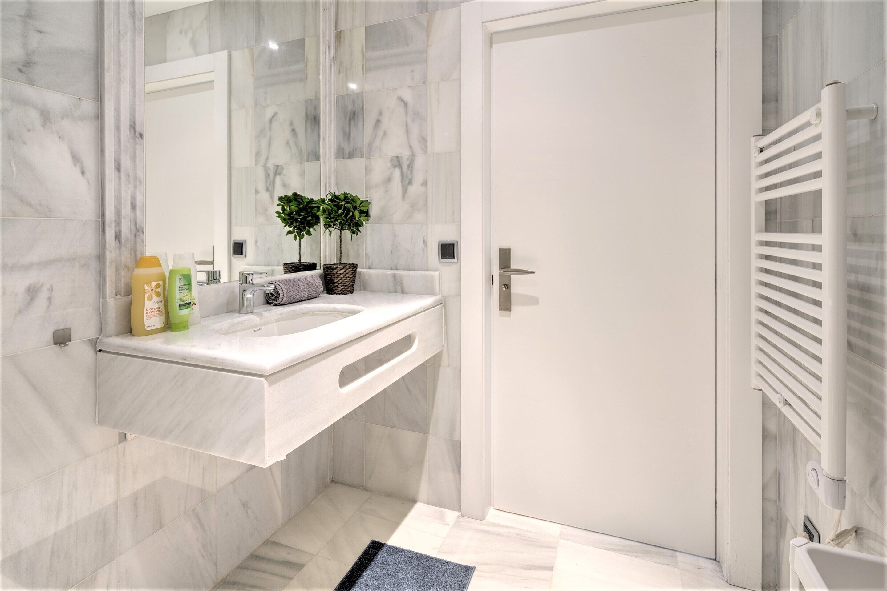 A modern bathroom with a marble sink, a mirror, a towel rack, and a white door.