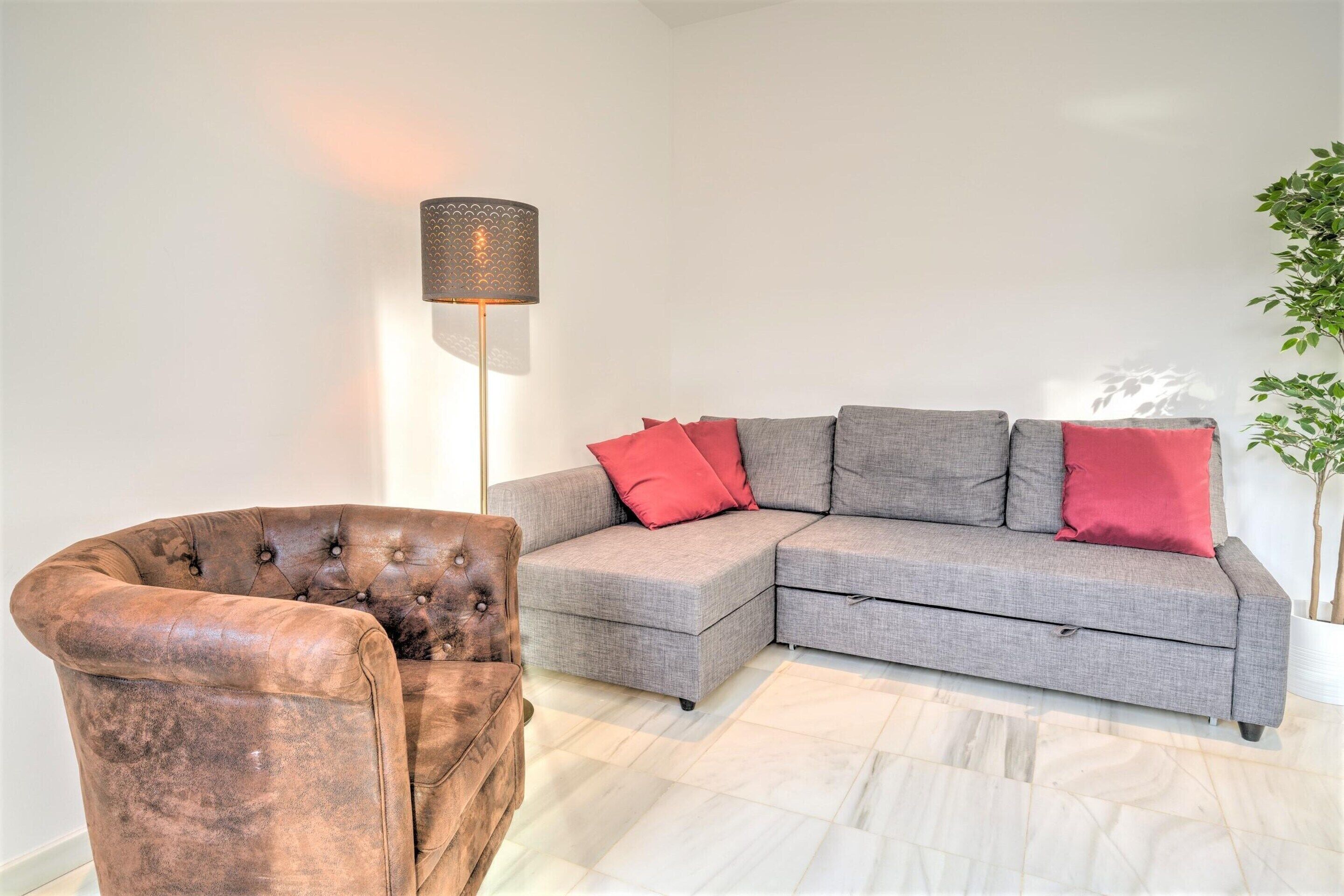 A living room with a grey sectional sofa, a brown armchair, and a floor lamp.