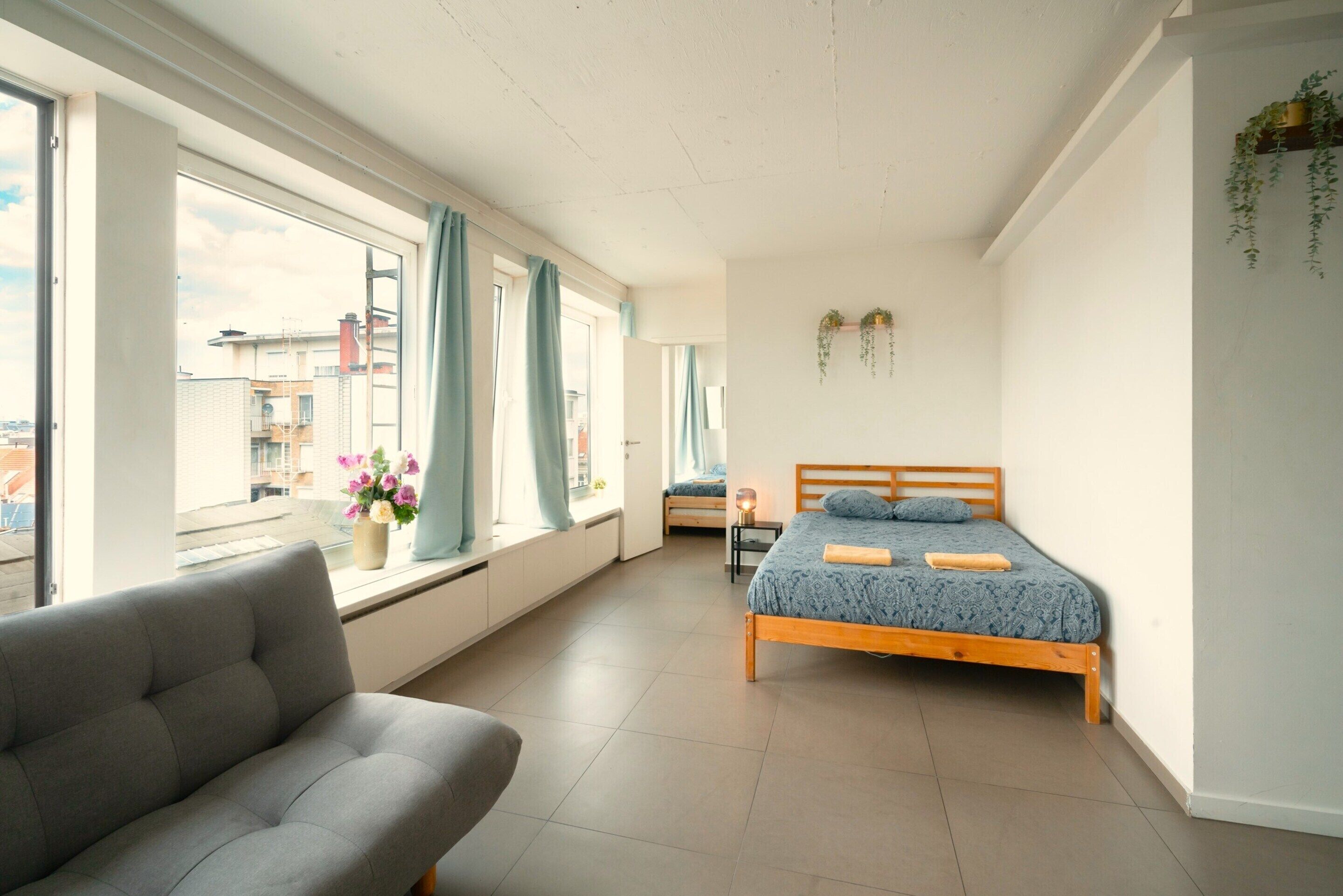Une chambre à coucher avec un lit, un canapé, une fenêtre avec des rideaux et une vue sur les bâtiments à l’extérieur.