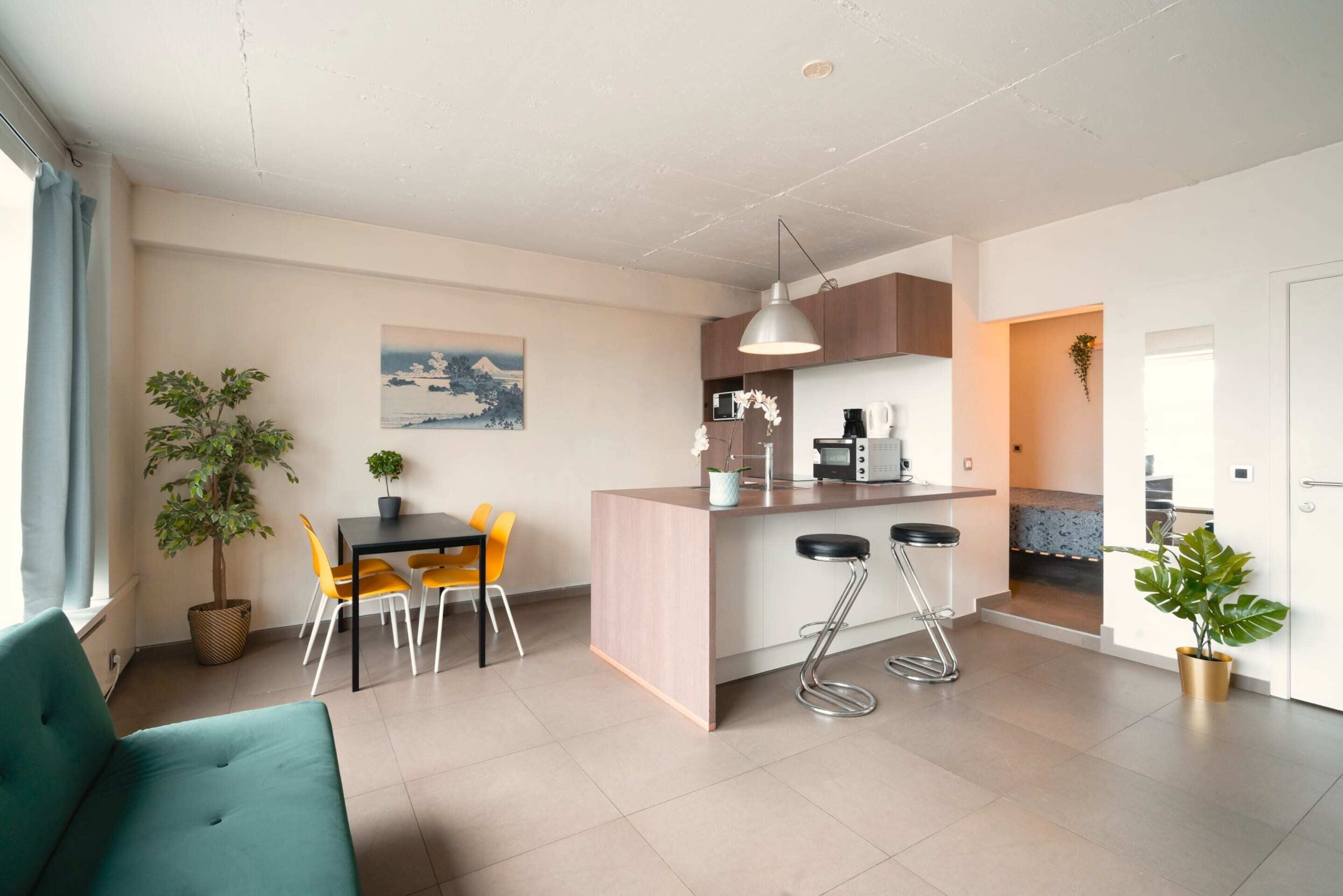A modern kitchen with a dining area, bar stools, and a large potted plant.