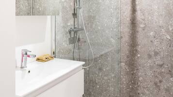 Un baño moderno con ducha acristalada, tocador blanco con espejo y salpicadero de mármol.
