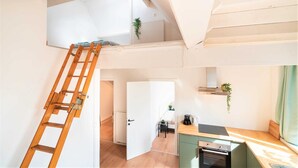 A loft-style apartment with a wooden ladder, a kitchenette, a bed, and a view of the outdoors.