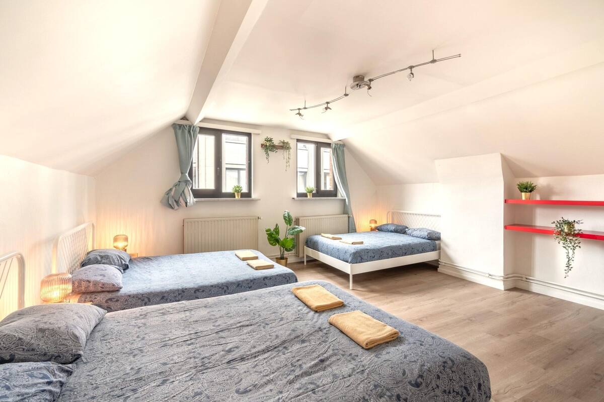 A bedroom with two beds, a red shelf, and a window with plants.