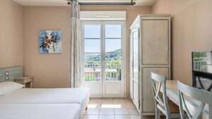 Een hotelkamer met een bed, een bureau, een stoel, een schilderij en een balkon met uitzicht.