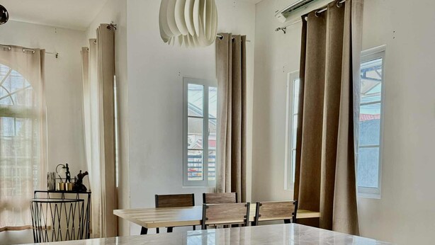 A modern kitchen with a marble countertop, a dining area with a table and chairs, and a large window with curtains. - Delightful 3-bedroom bungalow with AC in charming Dauis (Dauis)
