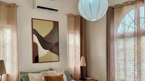 A neatly arranged bedroom with a bed, bedside lamps, a wall-mounted air conditioner, and a large window with curtains. - Delightful 3-bedroom bungalow with AC in charming Dauis (Dauis)