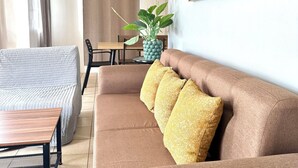 A living room with a brown sofa, a wooden coffee table, a grey armchair, a dining table with chairs, and a potted plant. - Delightful 3-bedroom bungalow with AC in charming Dauis (Dauis)