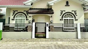 A two-story house with a gated entrance, a red-tiled roof, and a beige facade. - Delightful 3-bedroom bungalow with AC in charming Dauis (Dauis)