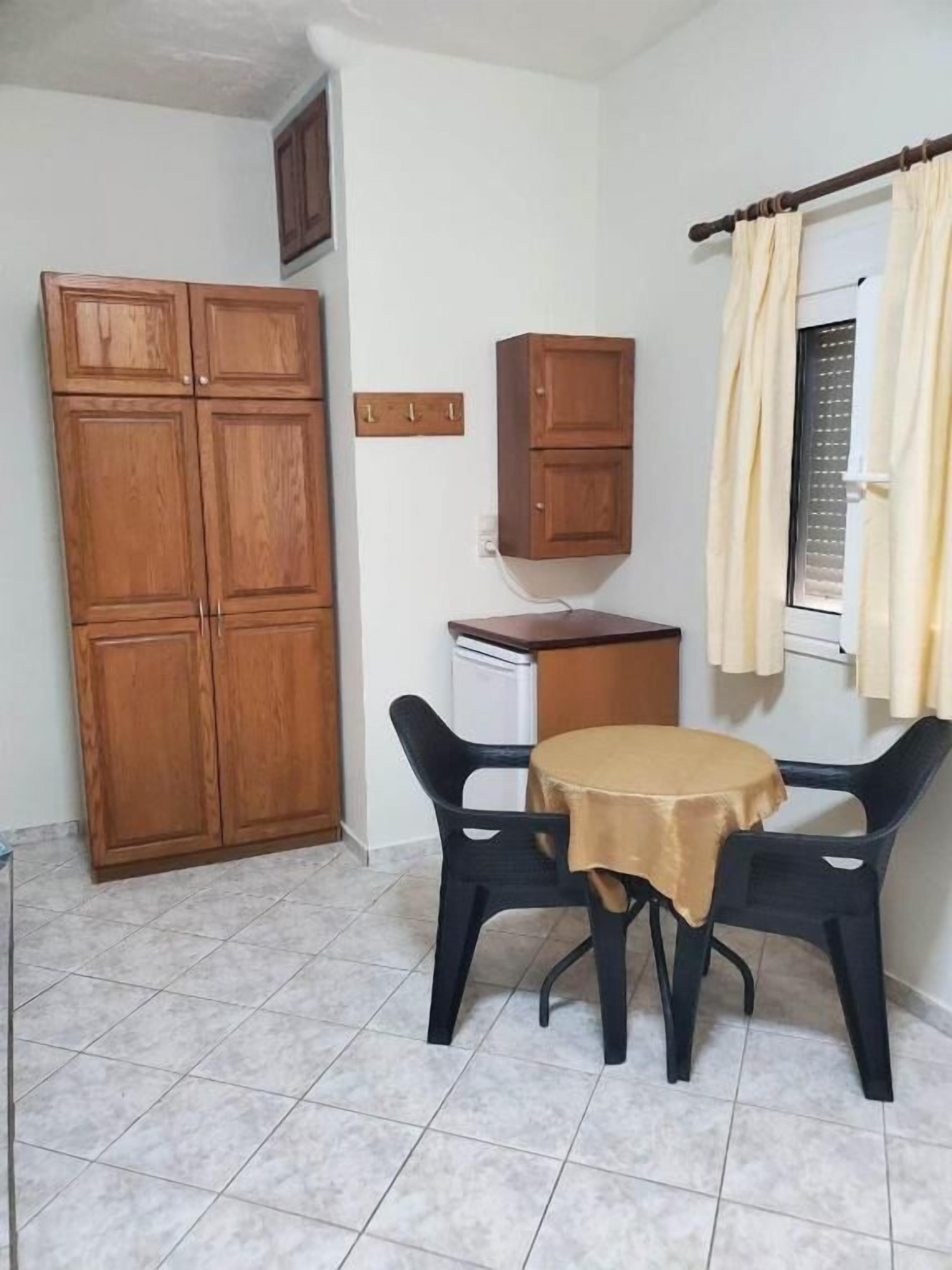 Een kleine kamer met een eettafel, twee stoelen, een kast en een raam met gordijnen.