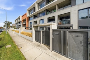 A modern multi-story building with balconies, a covered walkway, and utility meters. - Stylish 1-bed Retreat in Braddon (Canberra)
