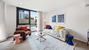 Ein modernes Wohnzimmer mit einer Couch, einem Sessel, einem Couchtisch und einem großen Fenster.