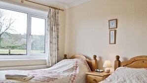 Quarto com duas camas, uma janela com cortinas, uma mesa de cabeceira com abajur e um quadro na parede.