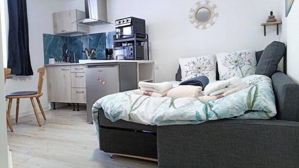 Een compacte slaapkamer met een bed, een klein bureau en een kitchenette.