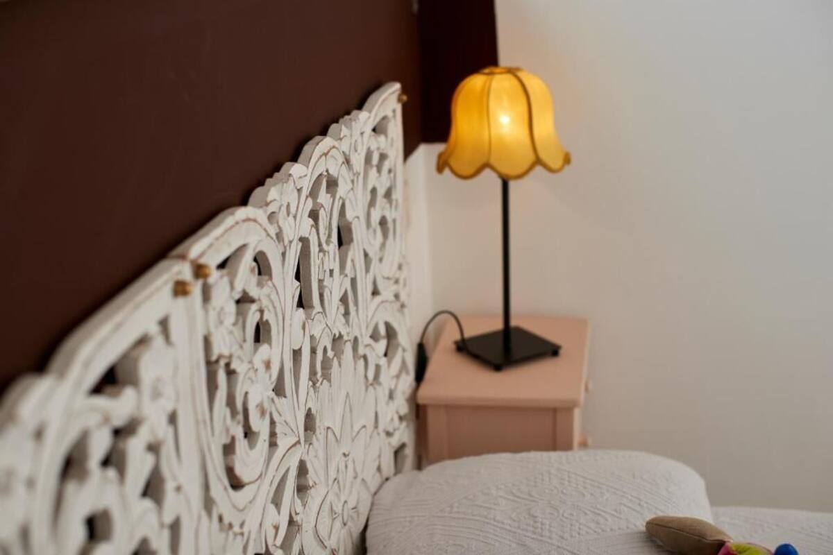 A bed with an ornate headboard, a bedside table with a lamp, and a small nightstand.