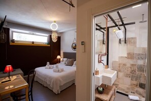 Habitación de hotel con cama, mesita de noche, lámpara y vistas a la zona de ducha.
