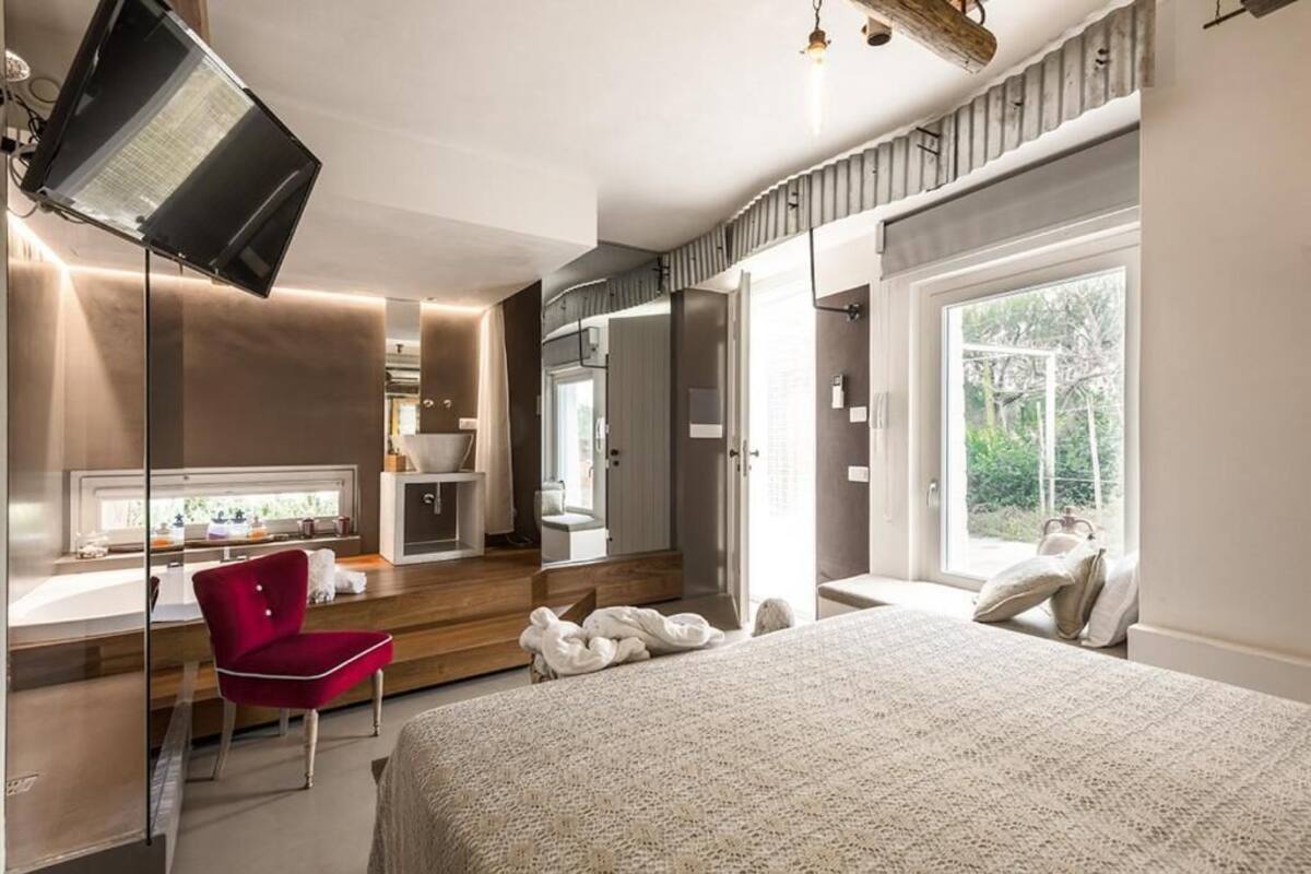 A modern bedroom with a large bed, a red chair, a desk, and a large window.