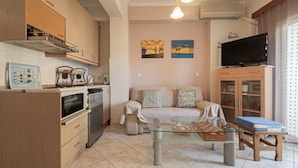 A compact living space with a kitchenette, a sofa, a coffee table, a TV, and a small dining area. - Goldie Home by RentalsPro - Kallithea Halkidiki (Kallithea)