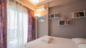 A hotel room with a bed, a window with curtains, a bookshelf, and a wall-mounted air conditioner. - Goldie Home by RentalsPro - Kallithea Halkidiki (Kallithea)