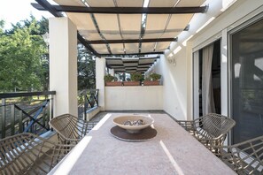 A covered outdoor patio with a table and chairs, a fire pit, and potted plants.