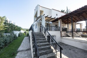 A two-story building with a stone staircase, outdoor seating area, and a pergola.