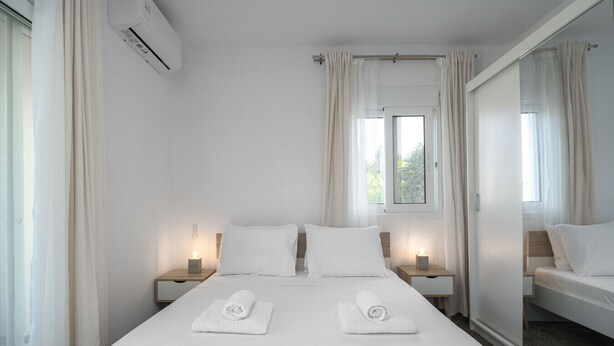 Ein Hotelzimmer mit einem großen Bett, zwei Nachttischen mit Lampen, einem Fenster mit Vorhängen und einem Spiegel an der Wand.