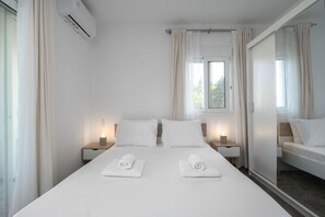 A hotel room with a large bed, two bedside tables with lamps, a window with curtains, and a mirror on the wall.