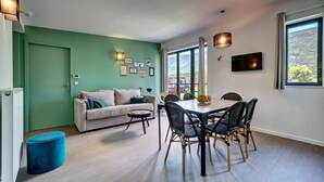 Een moderne woonkamer met een groene accentmuur, een witte bank, een eettafel met stoelen en een groot raam met uitzicht.