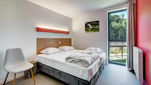 Een slaapkamer met een bed, een stoel, een schilderij en uitzicht op groen door een raam.