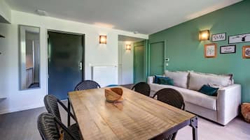 A modern living room with a wooden dining table, wicker chairs, a white sofa, and green walls.