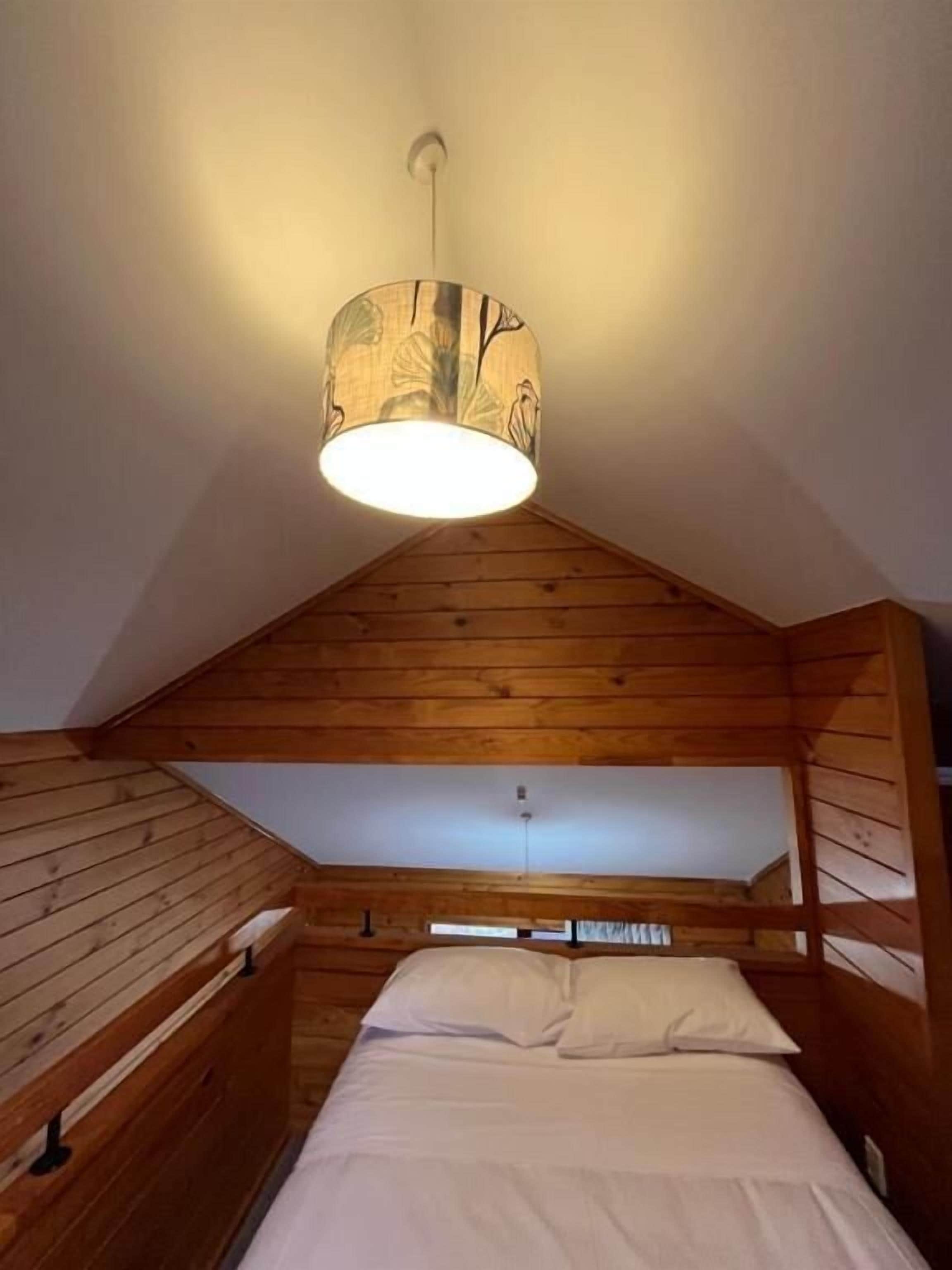 A room with wooden slatted walls, a bed with white bedding, and a hanging lamp with a patterned shade.