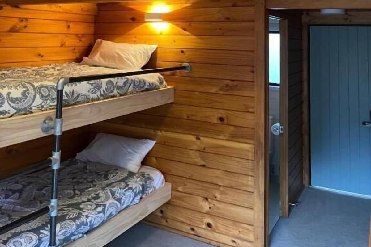 A bunk bed room with wooden walls, a ceiling light, and a door.