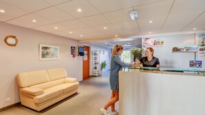 A reception area with a reception desk, a beige sofa, a framed painting, and a potted plant. - Coastal Apartment Near Beach for 4 (La Tranche-sur-Mer)