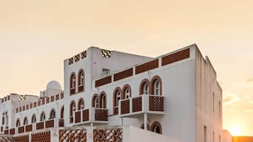 Un edificio de varios pisos con balcones y ventanas arqueadas, bajo un cielo al atardecer.
