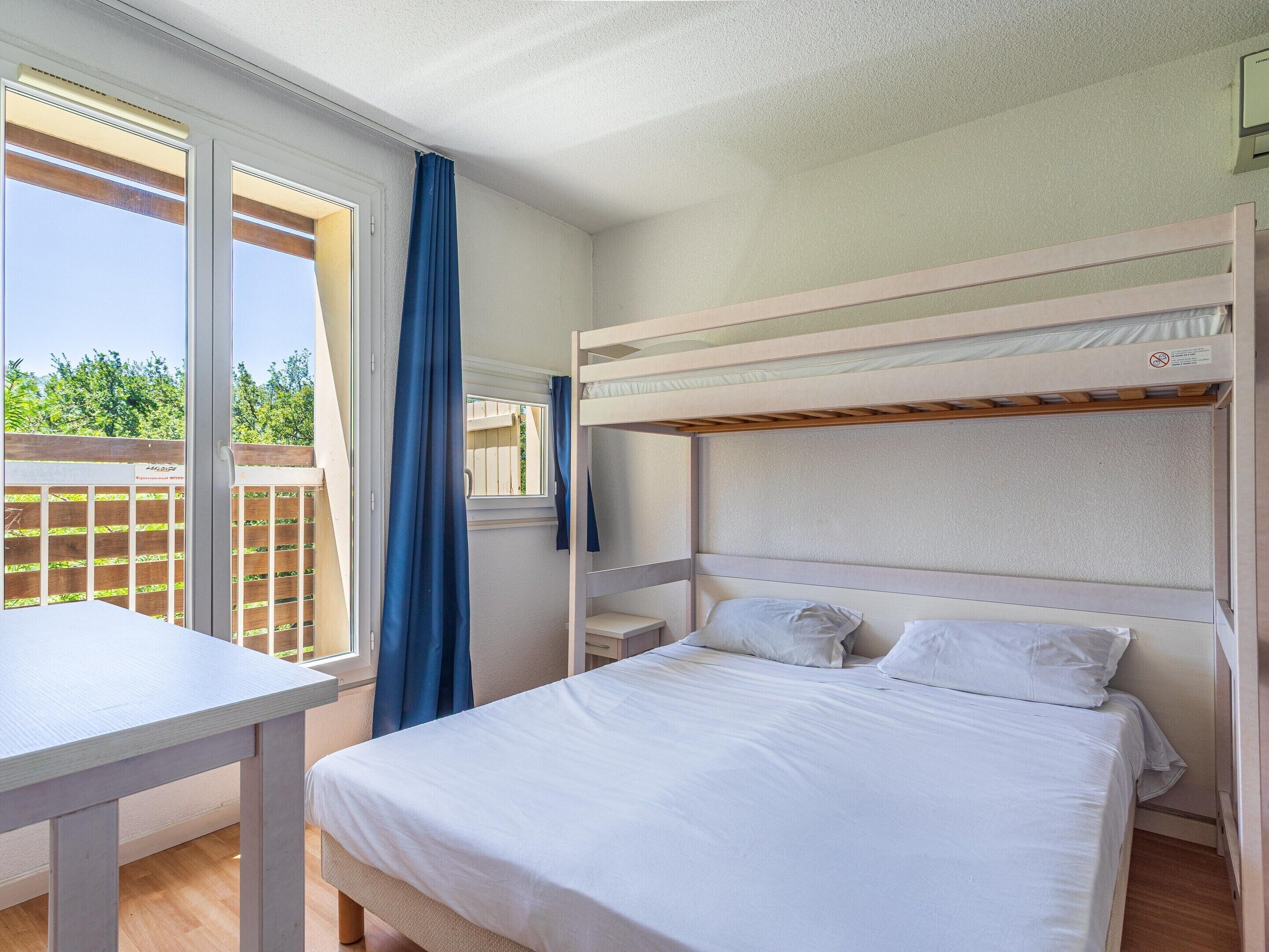 Een kamer met een stapelbed, een eenpersoonsbed, een tafel en een raam met gordijnen.